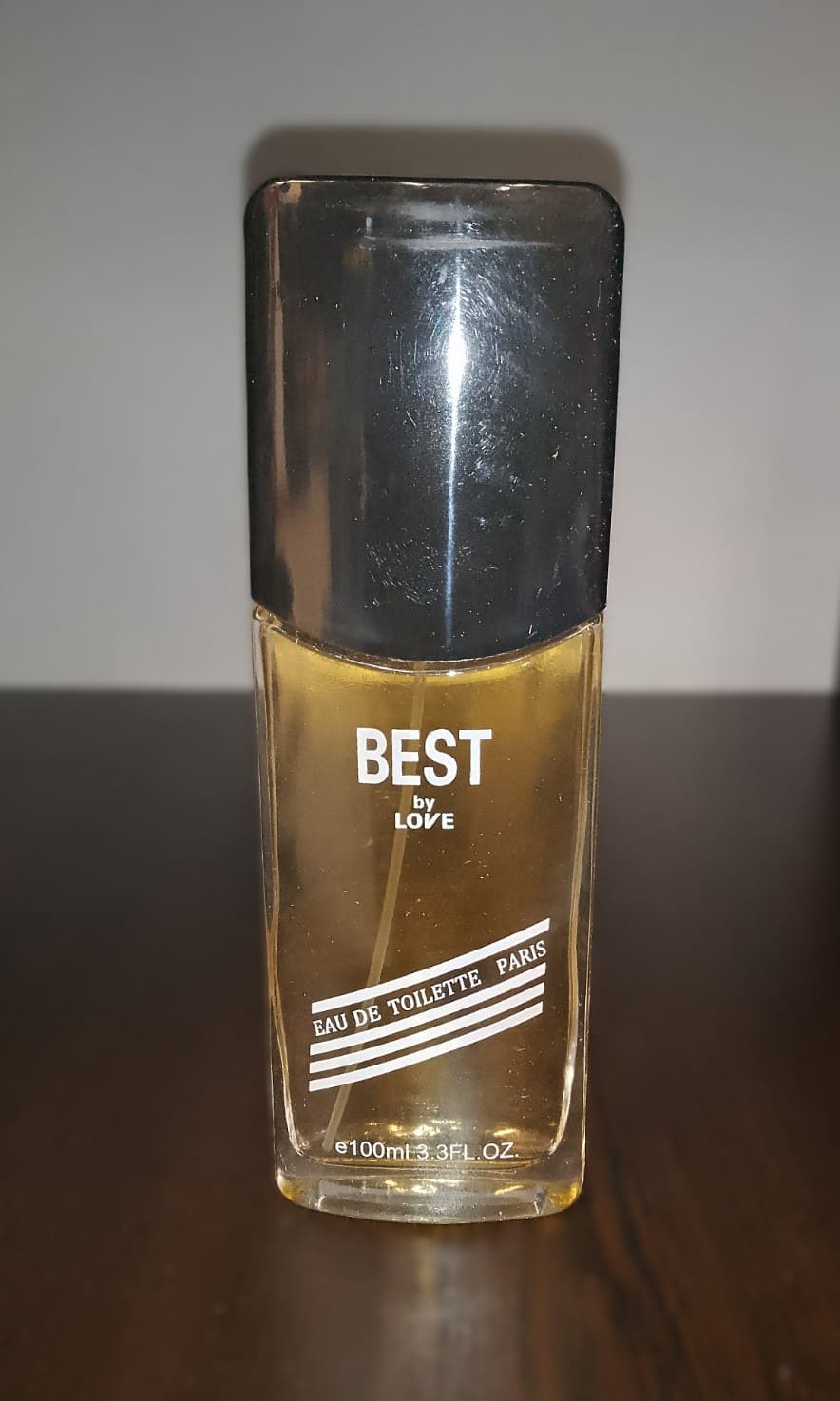 Парфюм "BEST by LOVE" с прозрачен флакон и златиста течност, поставен до оригиналната черна опаковка с декоративен дизайн.1