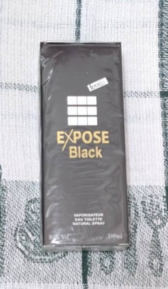 Мъжки парфюм EXPOSE Black в черна кутия с надпис в златисто, поставен върху зелено-бял текстилен фон.